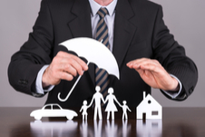 man in a suit holding a paper umbrella over paper cut outs of a family beside a home and car